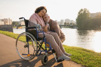 Older male caregiver hugging wife in wheelchair